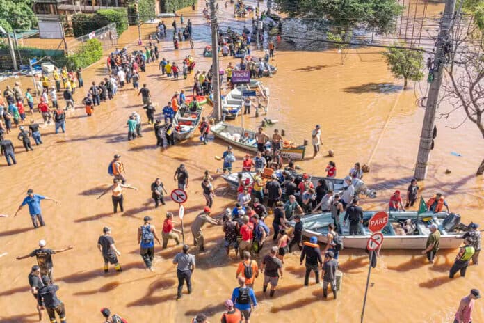 Foto de pessoas com água até as canelas, sendo ajudadas em barcos